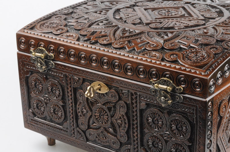 May include: A dark brown wooden box with intricate carvings and brass hinges. The box has a keyhole and a key in the lock. The box is decorated with a floral pattern.