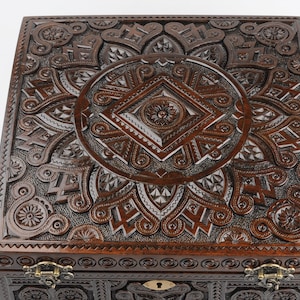 May include: A dark brown wooden box with intricate carvings on the lid and sides. The box has a brass lock and hinges.