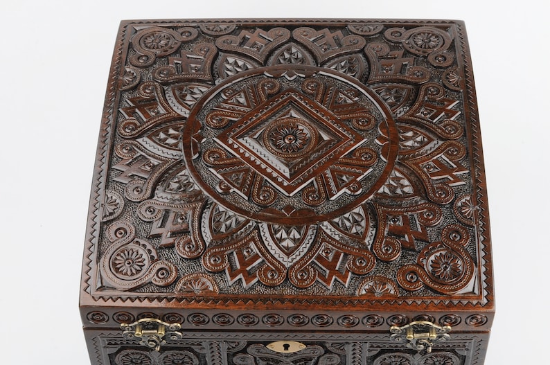 May include: A dark brown wooden box with intricate carvings on the lid and sides. The box has a brass lock and hinges.