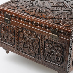 May include: A dark brown wooden box with intricate carvings and metal hinges. The box has a rounded top and sits on four small legs.