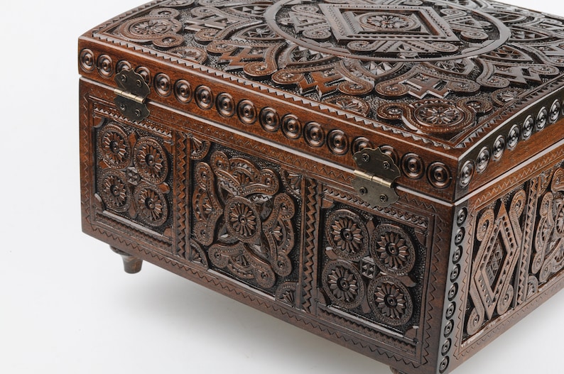 May include: A dark brown wooden box with intricate carvings and metal hinges. The box has a rounded top and sits on four small legs.
