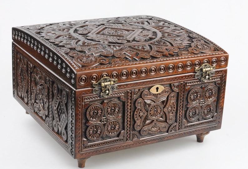 May include: A dark brown wooden box with intricate carvings and a brass lock. The box has a hinged lid and sits on four small legs.