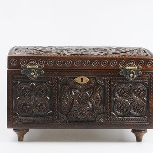 May include: A dark brown wooden box with intricate carvings and brass hinges. The box has a keyhole and sits on four small legs.