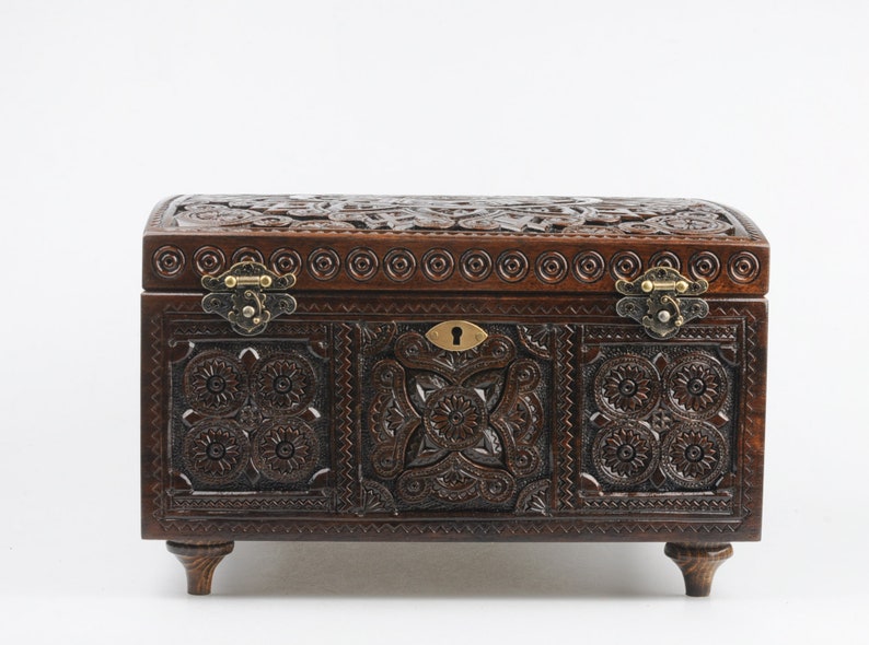 May include: A dark brown wooden box with intricate carvings and brass hinges. The box has a keyhole and sits on four small legs.