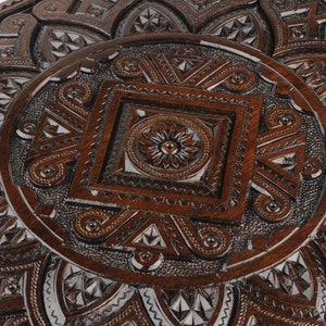 May include: A dark brown wooden box with intricate carved designs. The box has a square shape and a raised, circular design in the center.