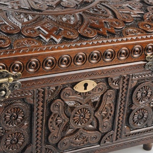 May include: A dark brown wooden box with intricate carvings and brass hinges. The box has a keyhole and a decorative design on the front.