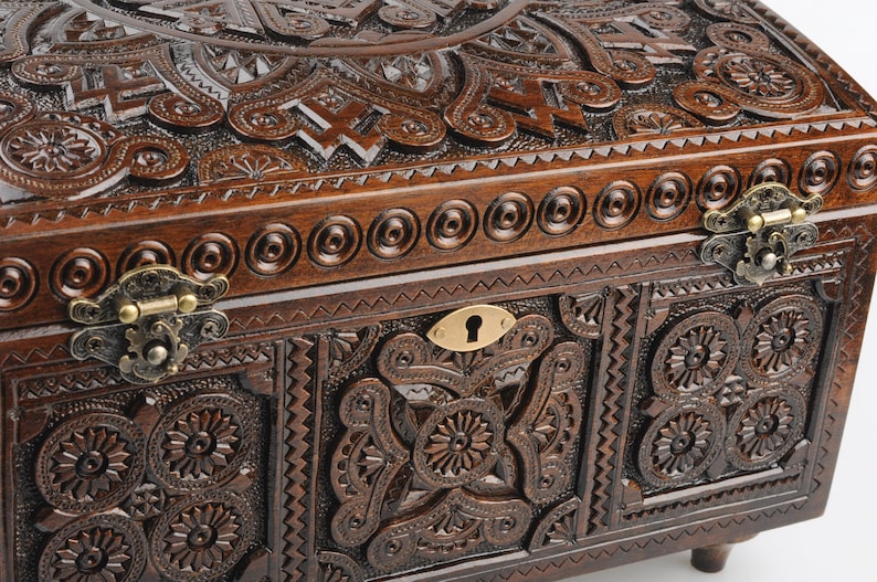 May include: A dark brown wooden box with intricate carvings and brass hinges. The box has a keyhole and a decorative design on the front.