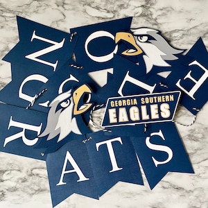 May include: A navy blue banner set with white letters spelling "CONGRATS" and a "Georgia Southern Eagles" logo. The banner features eagle head graphics. The letters are on pennant-shaped flags.