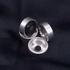 May include: Three silver metal rings, one with a black centre, stacked on a black surface.