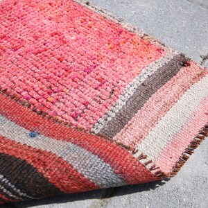 May include: A colorful striped rug with a pink, orange, brown, and white pattern. The rug is folded in half and has a frayed edge.