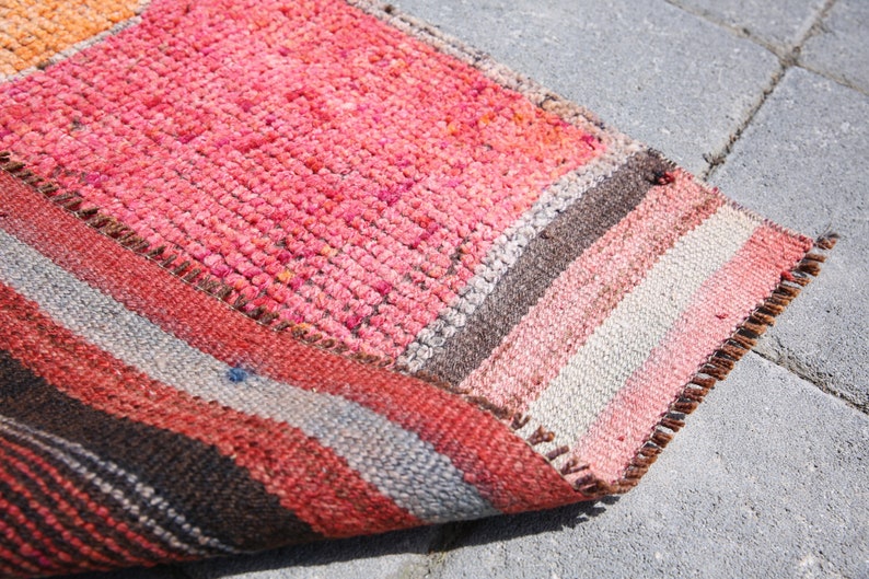 May include: A colorful striped rug with a pink, orange, brown, and white pattern. The rug is folded in half and has a frayed edge.