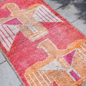 May include: A red, orange, and white patterned rug with a geometric design featuring stylized birds. The rug is made of woven fabric and has a distressed, vintage look.