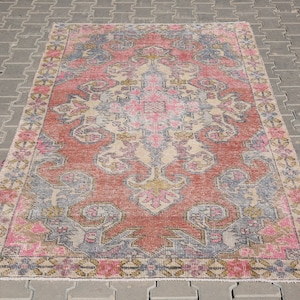 K&ouml;nnte beinhalten: Ein Vintage-Teppich mit einem verblassten rosa, beige und blauen floralen Muster. Der Teppich hat einen abgenutzten Look und ist perfekt, um jedem Raum einen Hauch von Boho-Stil zu verleihen.