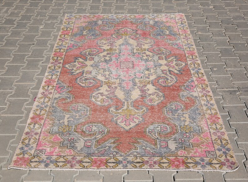 K&ouml;nnte beinhalten: Ein Vintage-Teppich mit einem verblassten rosa, beige und blauen floralen Muster. Der Teppich hat einen abgenutzten Look und ist perfekt, um jedem Raum einen Hauch von Boho-Stil zu verleihen.