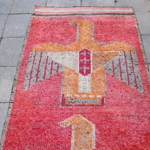 May include: A red, orange, and white rug with a stylized bird design. The rug has a fringed edge and is made of woven fabric.