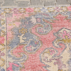 K&ouml;nnte beinhalten: Ein Vintage-Teppich mit einem verblassten rosa, blauen und goldenen floralen Muster. Der Teppich hat einen abgenutzten Look und ist aus einem weichen, gewebten Material gefertigt.