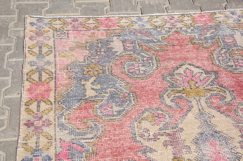 K&ouml;nnte beinhalten: Ein Vintage-Teppich mit einem verblassten rosa, blauen und goldenen floralen Muster. Der Teppich hat einen abgenutzten Look und ist aus einem weichen, gewebten Material gefertigt.