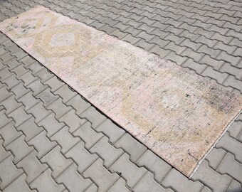Puede incluir: Una alfombra larga y rectangular con un patrón rosa y amarillo descolorido. La alfombra está sobre una superficie de hormigón gris.