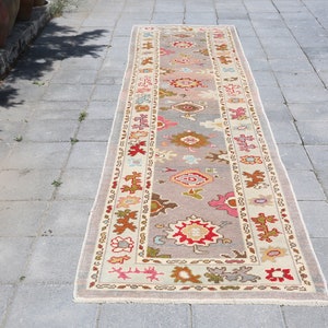 Puede incluir: Una alfombra larga y rectangular con fondo crema y un estampado floral colorido. La alfombra tiene un borde con un diseño geométrico.