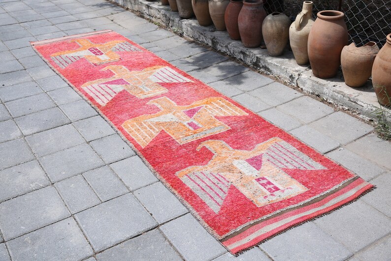 May include: A long, red runner rug with a geometric pattern of stylized birds in shades of orange, pink, and white. The rug is laid out on a gray concrete patio.