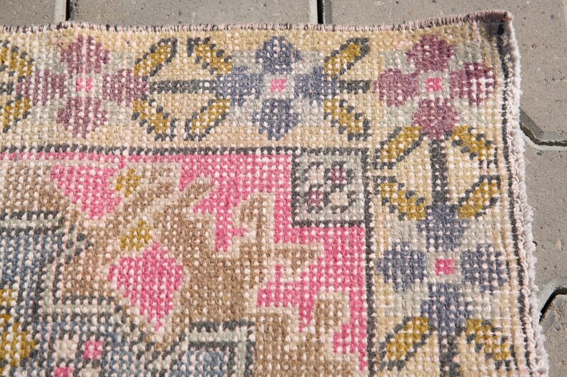 K&ouml;nnte beinhalten: Nahaufnahme eines gewebten Teppichs mit einem geometrischen Muster in Rosa-, Braun- und Graut&ouml;nen. Der Teppich hat einen Fransenrand.