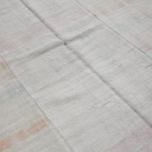 K&ouml;nnte beinhalten: Ein hellgrauer, rechteckiger Teppich mit Patchwork-Design. Der Teppich hat sichtbare N&auml;hte und dezente Flecken in Rosa, Orange und Blau. Die Textur wirkt weich und gewebt, geeignet f&uuml;r ein Wohn- oder Schlafzimmer.