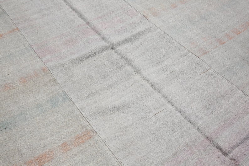 K&ouml;nnte beinhalten: Ein hellgrauer, rechteckiger Teppich mit Patchwork-Design. Der Teppich hat sichtbare N&auml;hte und dezente Flecken in Rosa, Orange und Blau. Die Textur wirkt weich und gewebt, geeignet f&uuml;r ein Wohn- oder Schlafzimmer.