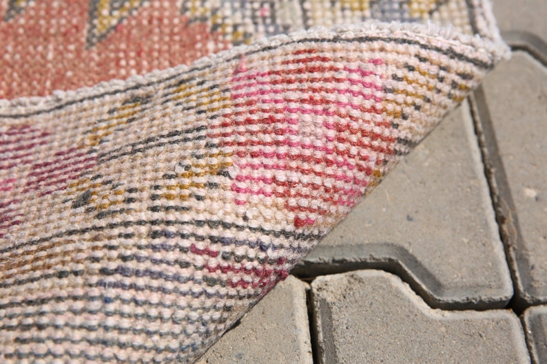 K&ouml;nnte beinhalten: Nahaufnahme eines beigefarbenen, rosa und goldfarbenen Teppichs mit gewebter Struktur. Der Teppich ist umgeklappt und die Unterseite ist sichtbar.