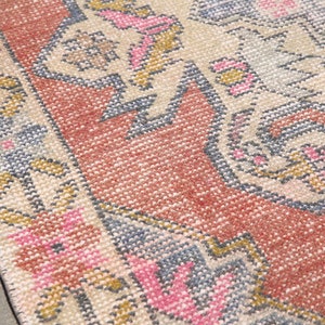 K&ouml;nnte beinhalten: Nahaufnahme eines Vintage-Teppichs mit einem floralen Muster in Rosa-, Blau- und Beiget&ouml;nen. Der Teppich hat einen abgenutzten Look und ist mit verschiedenen Texturen gewebt.