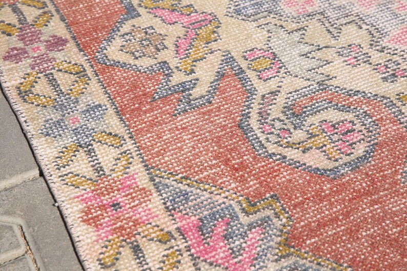 K&ouml;nnte beinhalten: Nahaufnahme eines Vintage-Teppichs mit einem floralen Muster in Rosa-, Blau- und Beiget&ouml;nen. Der Teppich hat einen abgenutzten Look und ist mit verschiedenen Texturen gewebt.