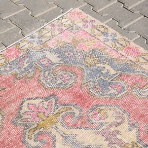 K&ouml;nnte beinhalten: Ein Vintage-Teppich mit einem floralen Muster in Rosa, Beige und Blau. Der Teppich hat einen abgenutzten Look und ist aus einem weichen, gewebten Material gefertigt.