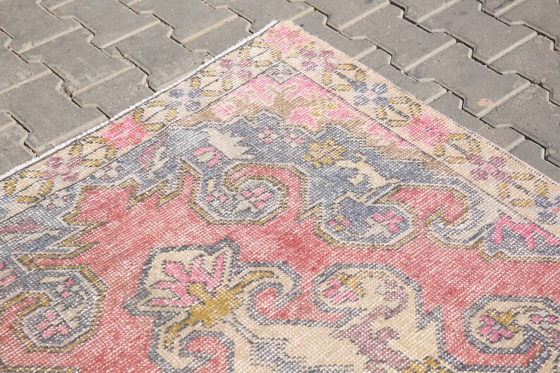 K&ouml;nnte beinhalten: Ein Vintage-Teppich mit einem floralen Muster in Rosa, Beige und Blau. Der Teppich hat einen abgenutzten Look und ist aus einem weichen, gewebten Material gefertigt.