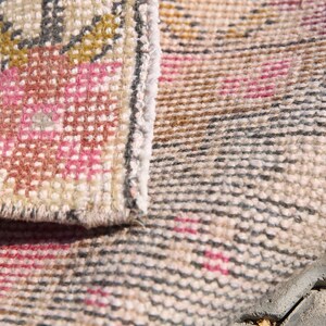 K&ouml;nnte beinhalten: Nahaufnahme eines beige-rosa gemusterten Teppichs mit gewebter Textur. Der Teppich ist in der Mitte gefaltet, sodass die Unterseite des Teppichs sichtbar ist.