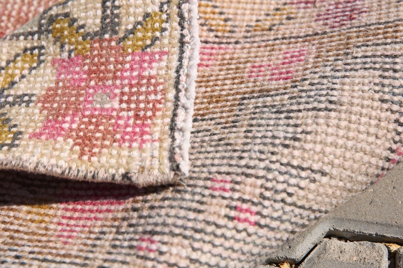 K&ouml;nnte beinhalten: Nahaufnahme eines beige-rosa gemusterten Teppichs mit gewebter Textur. Der Teppich ist in der Mitte gefaltet, sodass die Unterseite des Teppichs sichtbar ist.