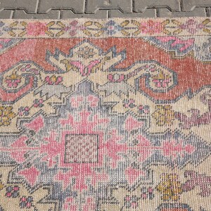 K&ouml;nnte beinhalten: Ein Vintage-Teppich mit einem verblassten rosa, blauen und beigen Muster. Der Teppich hat ein traditionelles Design mit komplizierten Details und einem zentralen Medaillon.