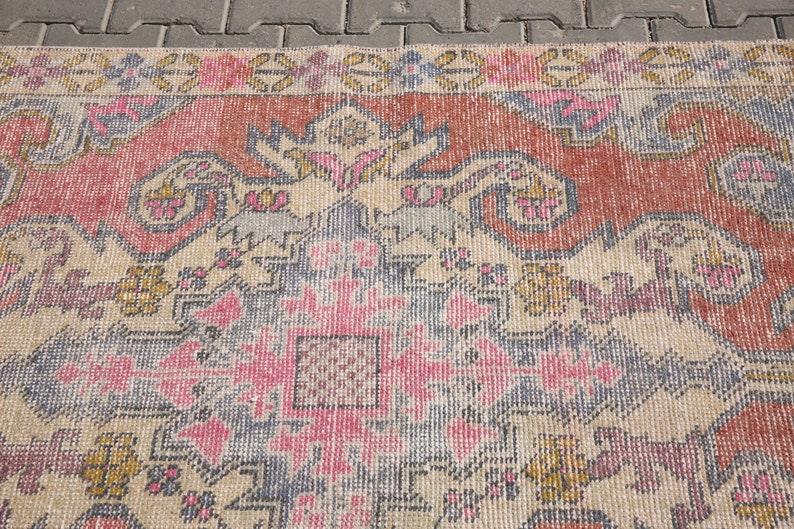 K&ouml;nnte beinhalten: Ein Vintage-Teppich mit einem verblassten rosa, blauen und beigen Muster. Der Teppich hat ein traditionelles Design mit komplizierten Details und einem zentralen Medaillon.