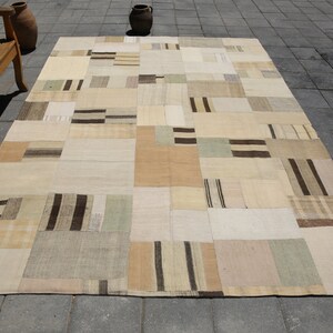 May include: A patchwork rug with a beige, brown, and white color scheme. The rug is made of different fabrics and has a variety of patterns, including stripes and squares.