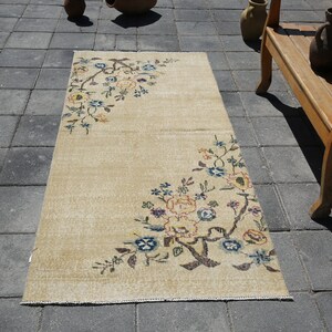 May include: A beige runner rug with a floral design in shades of blue, yellow, and brown. The rug has a distressed look and is perfect for adding a touch of vintage charm to any room.