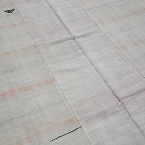 K&ouml;nnte beinhalten: Ein hellfarbiger, rechteckiger Teppich mit strukturierter Oberfl&auml;che. Der Teppich weist verblasste orangefarbene und schwarze horizontale Streifen und kleine geometrische Muster auf. Der Teppich besteht aus gewebtem Material.