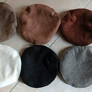 Può includere: Una collezione di sei cappelli Pakol in vari colori: marrone chiaro, marrone medio, marrone scuro, bianco, nero e grigio. Questi cappelli tradizionali a cupola rotonda sono esposti su una superficie piastrellata.
