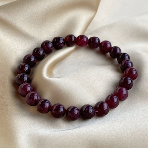 Puede incluir: Un brazalete de piedras preciosas de color morado oscuro con cuentas redondas. El brazalete está hecho de piedras naturales y es un hermoso accesorio para cualquier ocasión.
