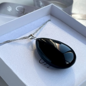 May include: A silver chain necklace with a black teardrop-shaped pendant. The pendant is smooth and shiny.