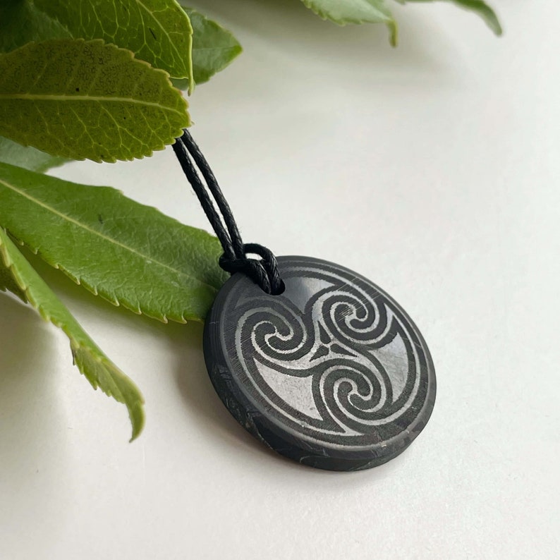Puede incluir: Collar con colgante negro con un dise&ntilde;o de nudo celta plateado. El colgante es redondo y tiene un cord&oacute;n negro.