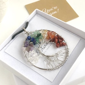 May include: A silver wire wrapped tree of life pendant with seven chakra stones. The stones are amethyst, lapis lazuli, green aventurine, citrine, carnelian, red jasper, and clear quartz. The pendant is in a white gift box with a card that says "You're a gem!"