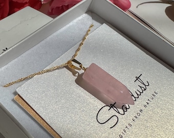 Può includere: Collana con pendente in cristallo di quarzo rosa e catena color oro. Il pendente è un cristallo allungato rosa chiaro. La collana è presentata in una scatola bianca con la scritta "Stardust" e "Gifts From Nature".