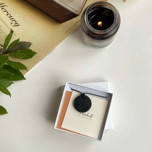 Puede incluir: Un collar negro con un colgante redondo que presenta un dise&ntilde;o de nudo celta. El colgante est&aacute; en una caja blanca con una tarjeta que dice "Stardust Gifts from Nature".