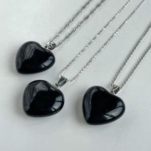 May include: Three necklaces featuring polished, smooth, black heart-shaped pendants suspended from thin, silver-toned metal chains. Each pendant is securely attached to the chain with a small, metallic bail, showcasing a glossy, reflective surface.