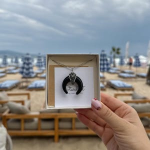 May include: A silver-toned necklace featuring a black crescent moon pendant with a small cluster of clear crystals at the top. The necklace is presented on a white card with the text Stardust Gifts from Nature inside a white box.