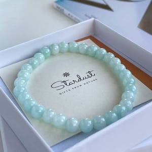 Peut inclure: Un bracelet en pierres précieuses bleu clair avec des perles rondes dans une boîte blanche avec une carte blanche qui dit "Stardust Gifts from Nature".