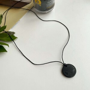 Puede incluir: Un collar negro con un colgante redondo con un dise&ntilde;o de nudo celta tallado.
